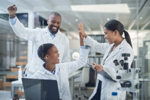 Shot of a group of young scientists giving each other a high five while using a laptop in a laboratory